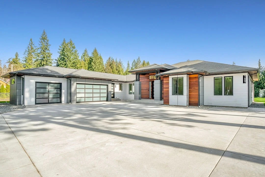 Modern home exterior with glass-panel garage doors and a wide driveway