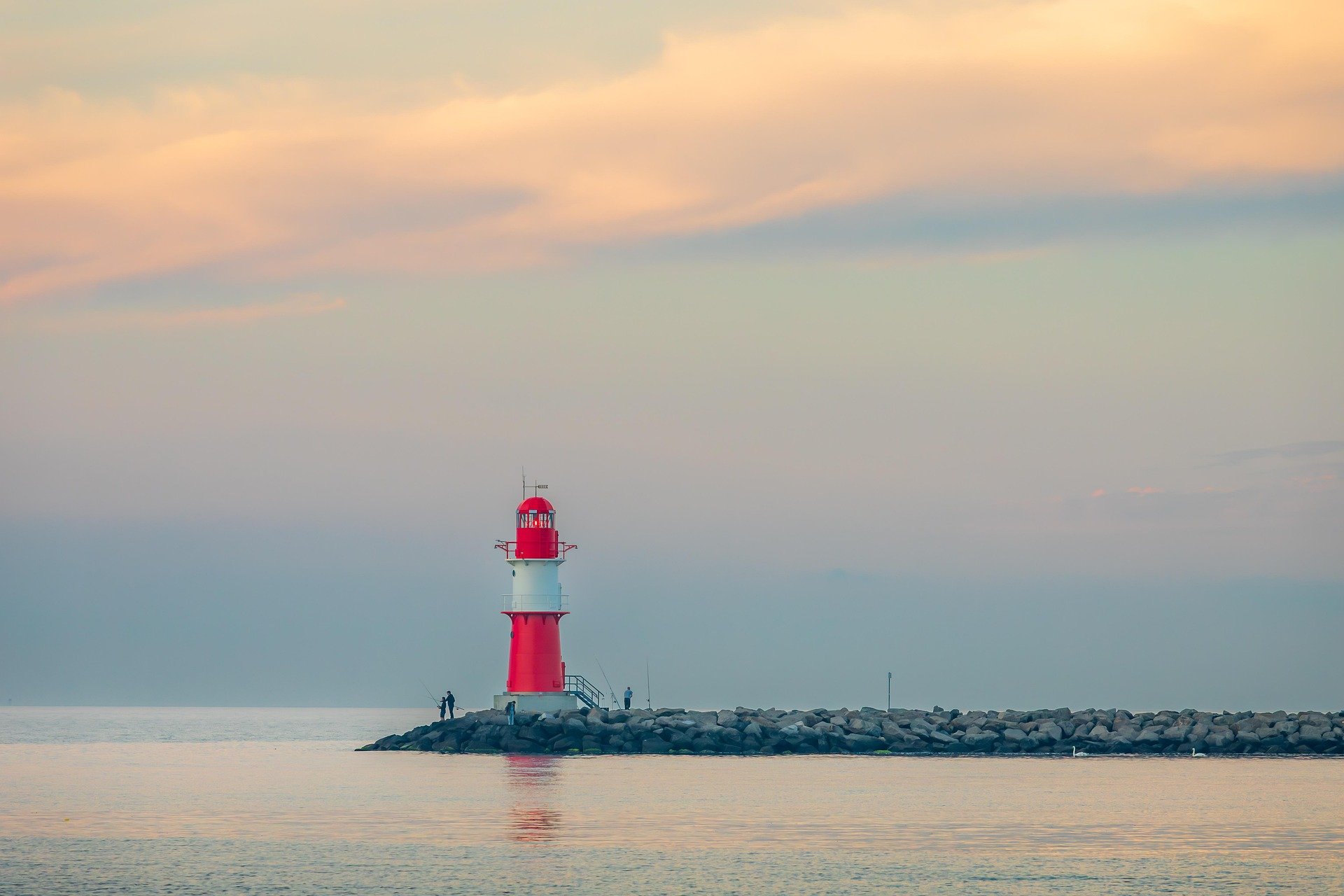 Red lighthouse on a calm shoreline at sunrise.