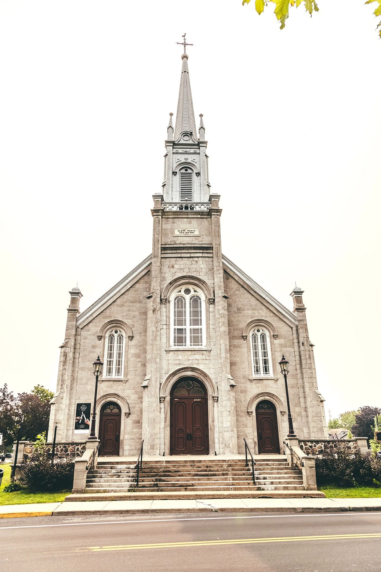 Église Sainte-Trinité-de-Contrecoeur — modern exterior showing the stone facade, central arched windows, three arched doorways, and tall steeple with cross