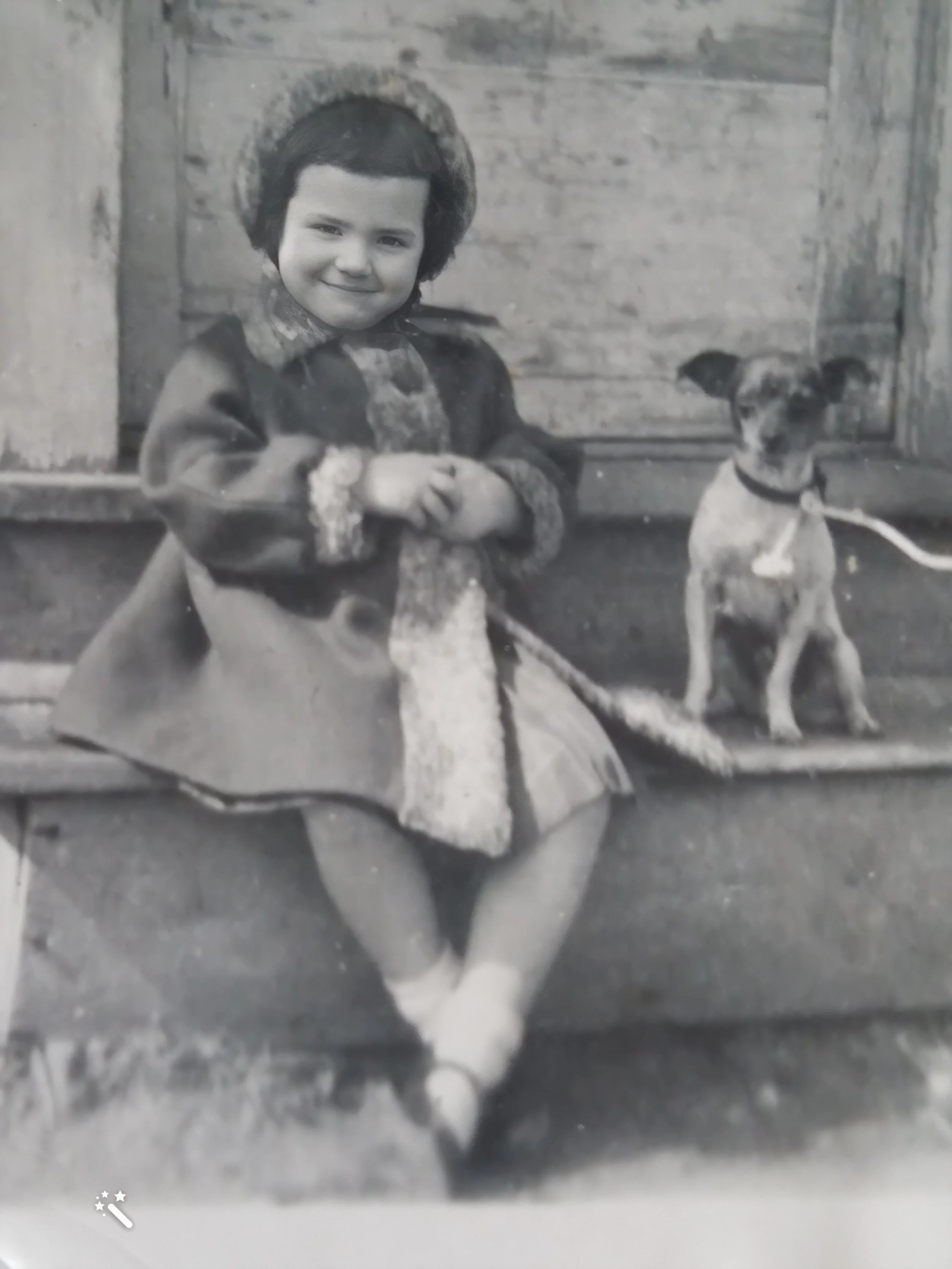 Judy Robertson as a young girl in Montclair, wearing a fur-trimmed bonnet and coat, seated on a stoop with a small terrier