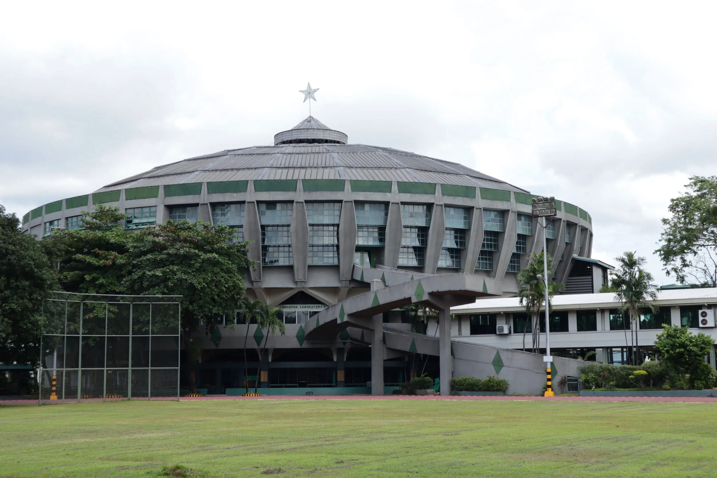 Aerial view of the La Salle Green Hills campus in Mandaluyong, the green-roofed buildings and domed St. Benilde Gym set against the Metro Manila skyline
