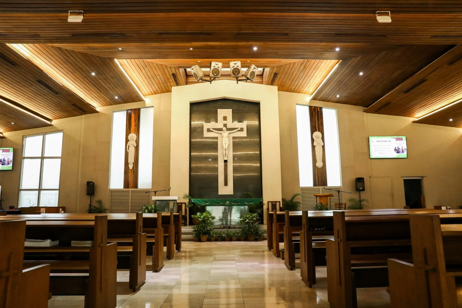 The interior of a La Salle Green Hills chapel, with a large crucifix above the altar and wooden pews along a polished aisle