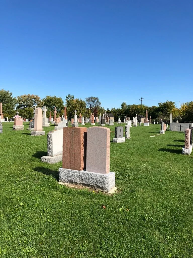 The cemetery at Saint-Constant under a clear blue sky, rows of grave markers on green grass