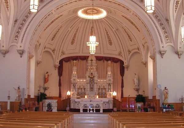Sainte-Trinité-de-Contrecoeur interior — barrel-vaulted ceiling with ornamental plasterwork, white walls, and ornate altar with red curtains