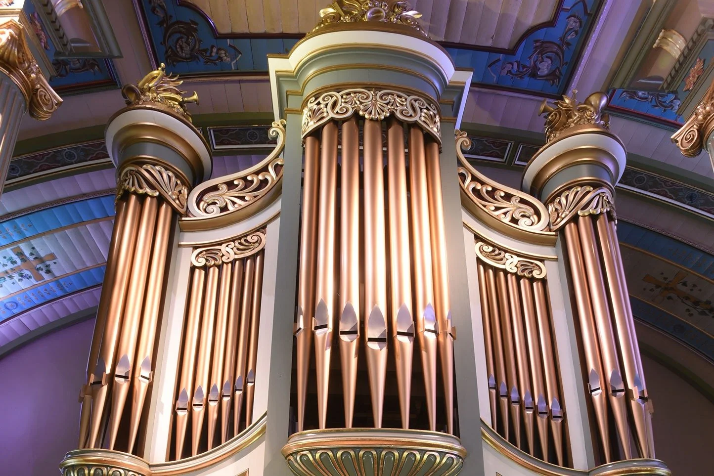 Close-up of the Casavant organ pipes at Sainte-Famille Church, gleaming copper against the painted ceiling