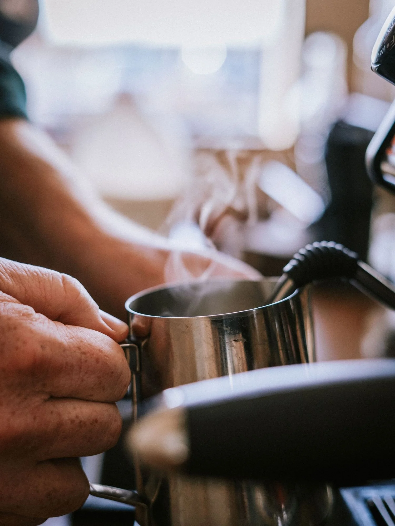 Steam rising from a milk pitcher at the espresso machine