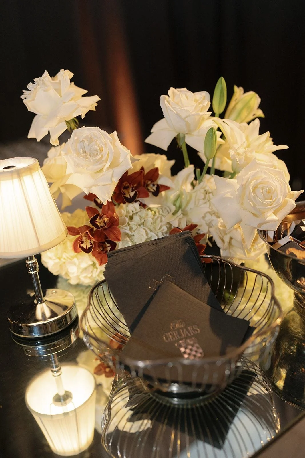 Ivory roses and lilies beside a glowing table lamp at the reception