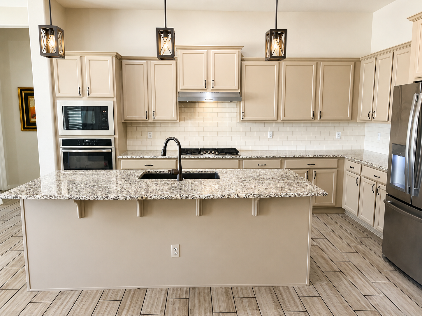 Cream painted kitchen cabinets with black pulls, granite island, and pendant lights