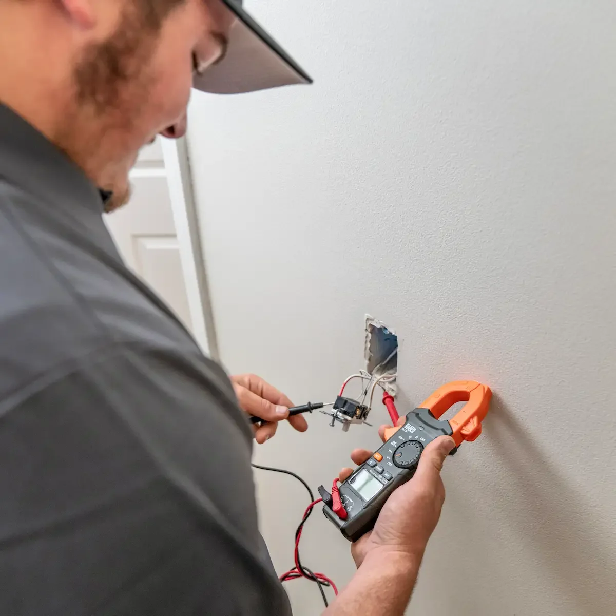 A Miracle Electric electrician tests the wiring in an open outlet box with a clamp meter and probes.