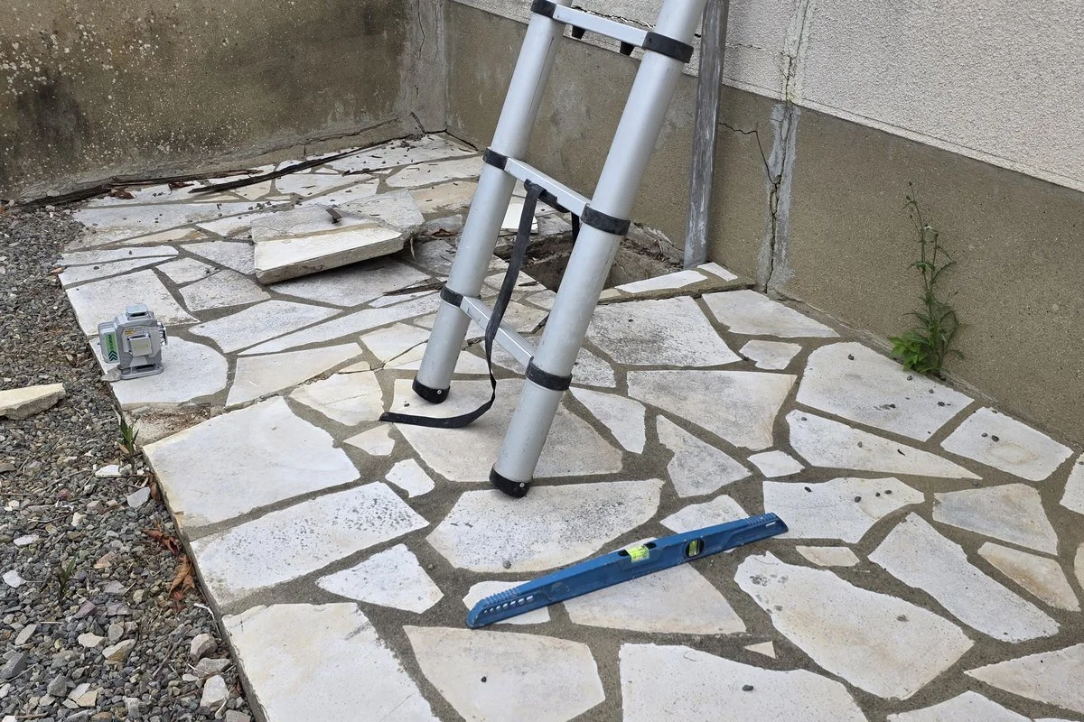 Échelle télescopique, niveau et laser posés au pied d&rsquo;une façade avant relevé