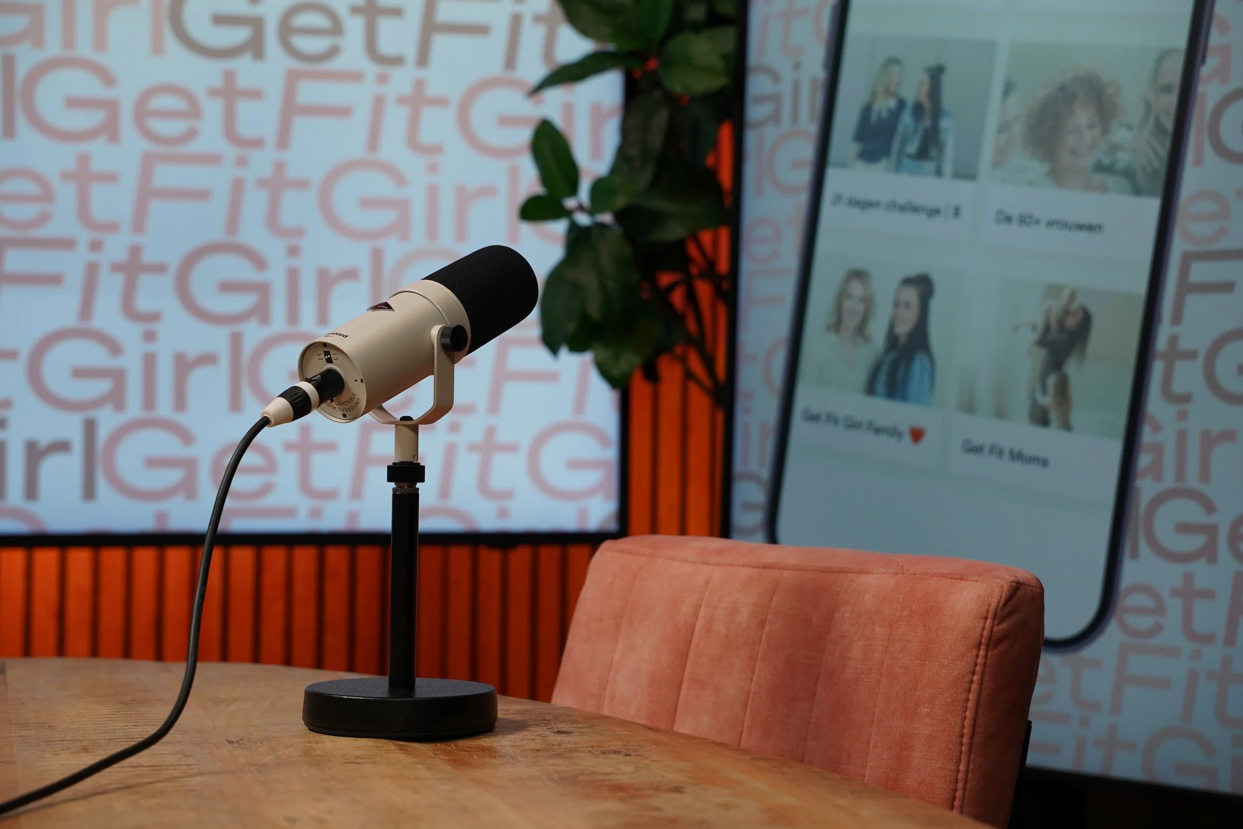 Podcastmicrofoon op de opnametafel met de branding van een klant op het scherm erachter