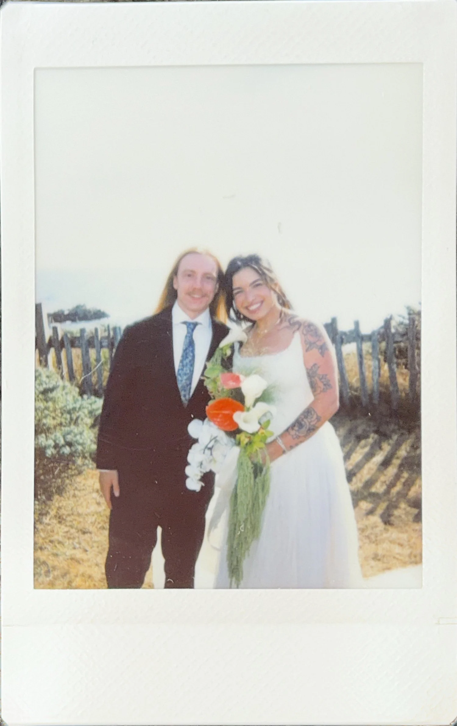 Instant photo of the couple by a wooden fence on the coast