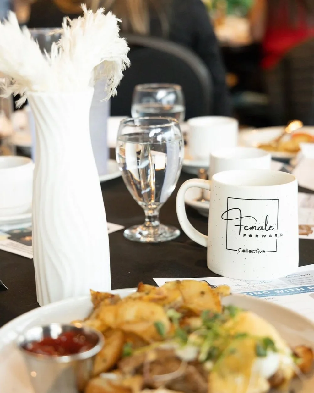 A Female Forward Collective place setting with a branded mug and breakfast