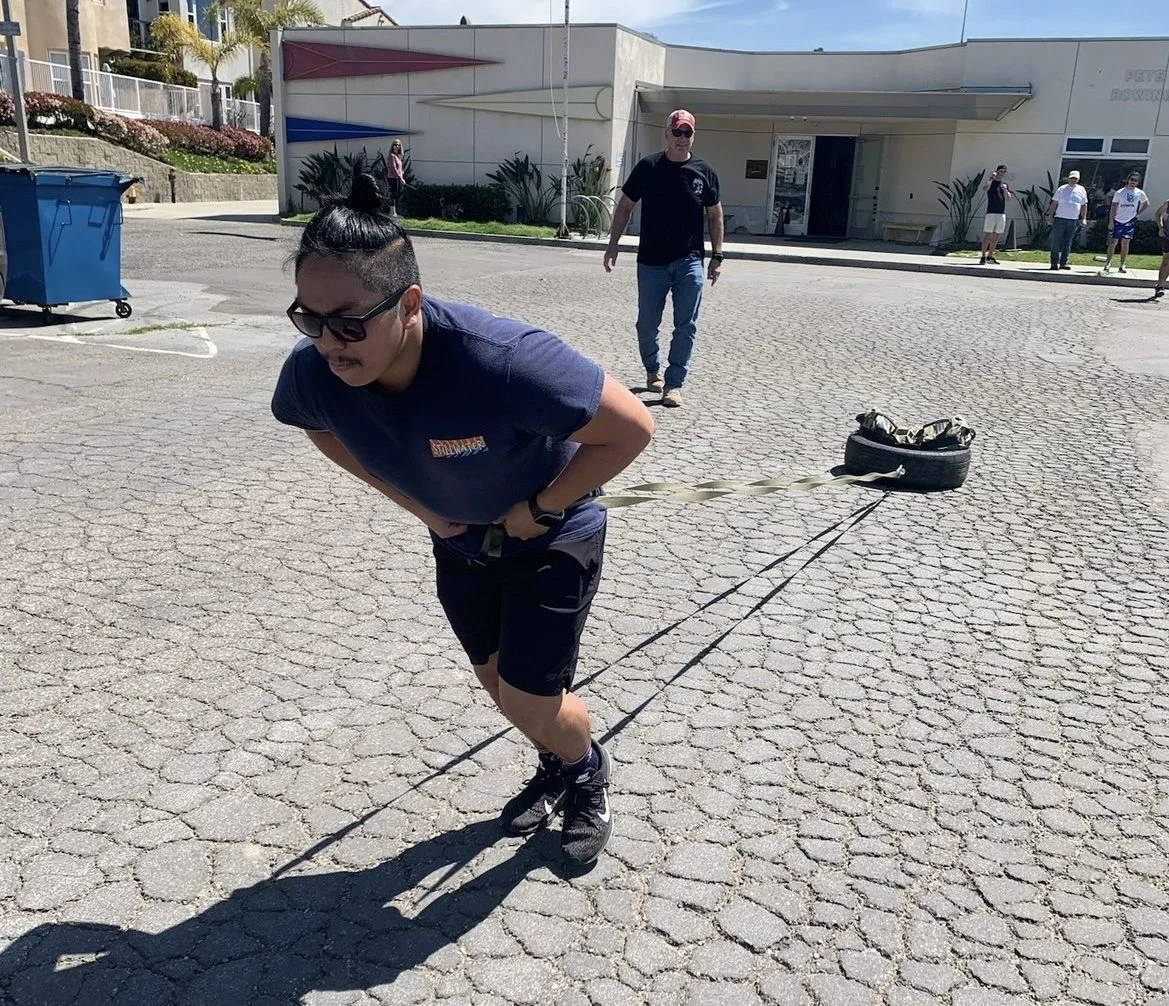 Novice rower, Gillan, pulling the tire across the parking lot with Coach Scott supervising.