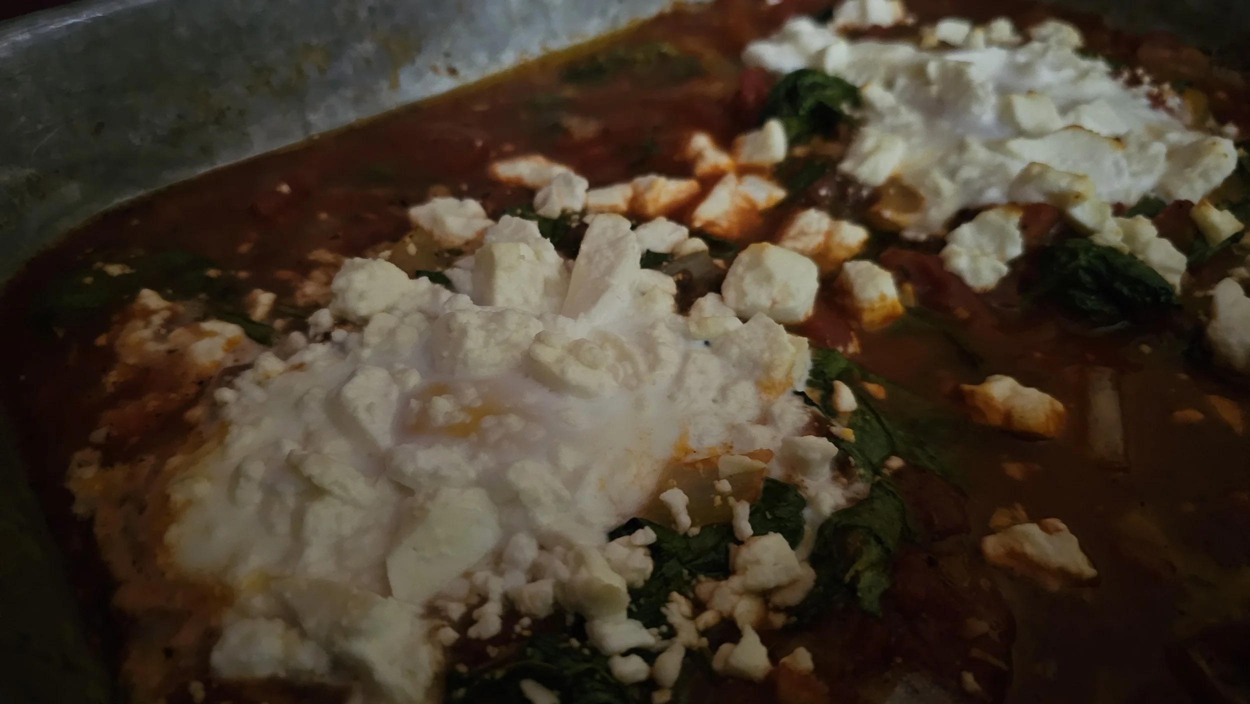 Skillet with eggs and cheese crumbled on top, ready for baking.