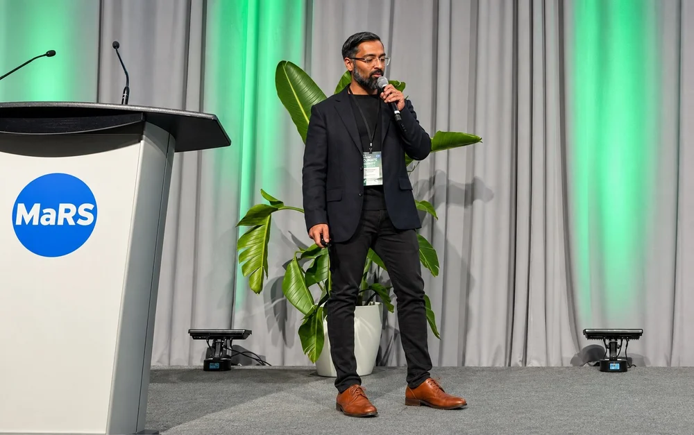 Prashant Jairaj speaking on stage with a handheld microphone