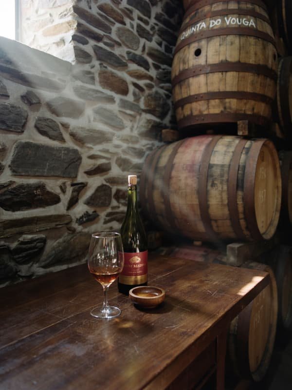 A glass of tawny port on a worn wooden table in a schist-walled Douro cellar with oak casks behind