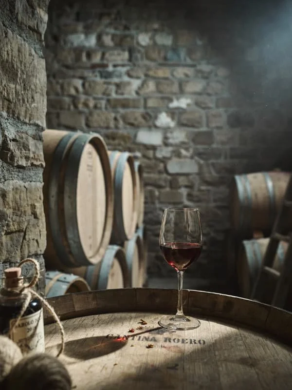 Glass of Nebbiolo wine resting on an oak barrel in a Piedmont cellar