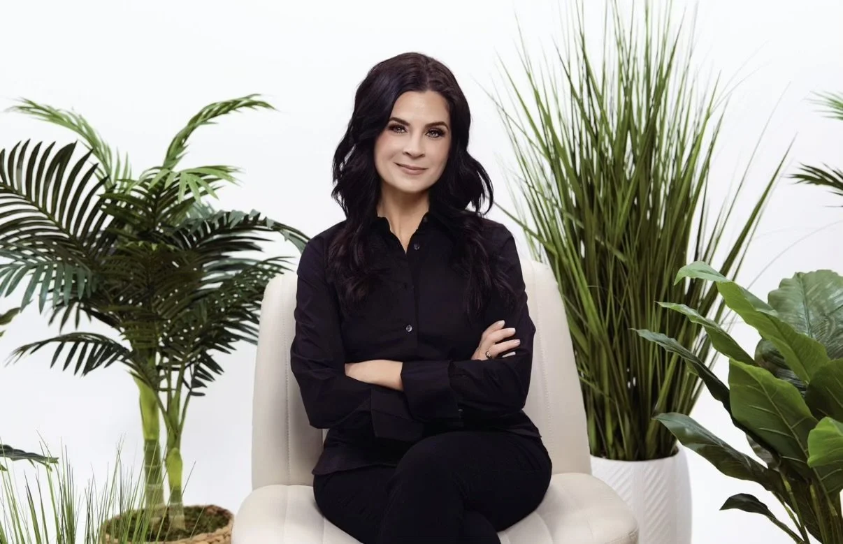 Jessica Lodato seated in a cream armchair, arms folded, surrounded by green plants