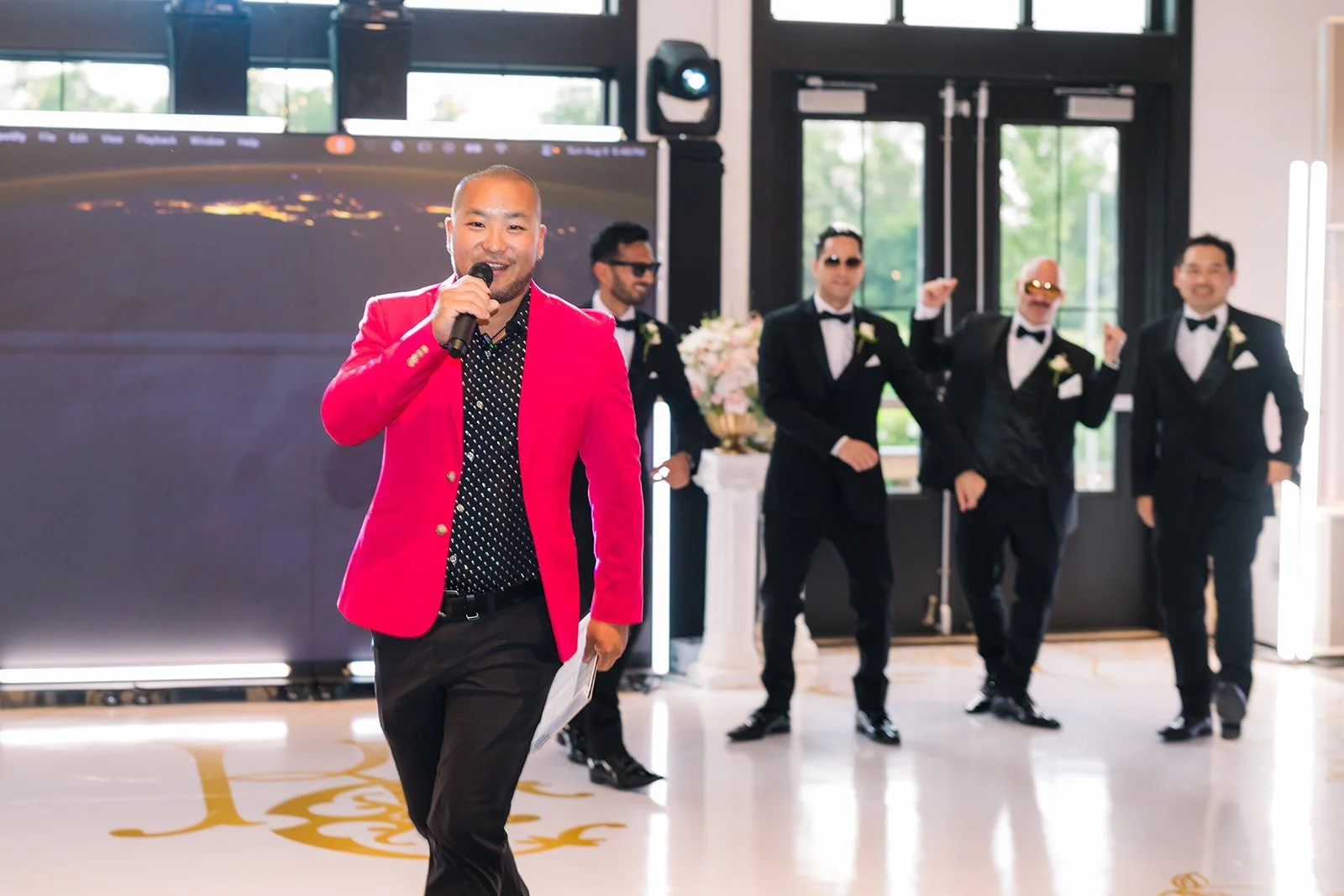 DJ Washburn hosting a wedding in a bright red jacket with the wedding party behind him