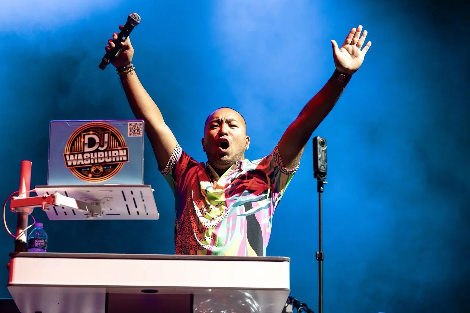 DJ Washburn on stage with both arms raised beneath blue lights