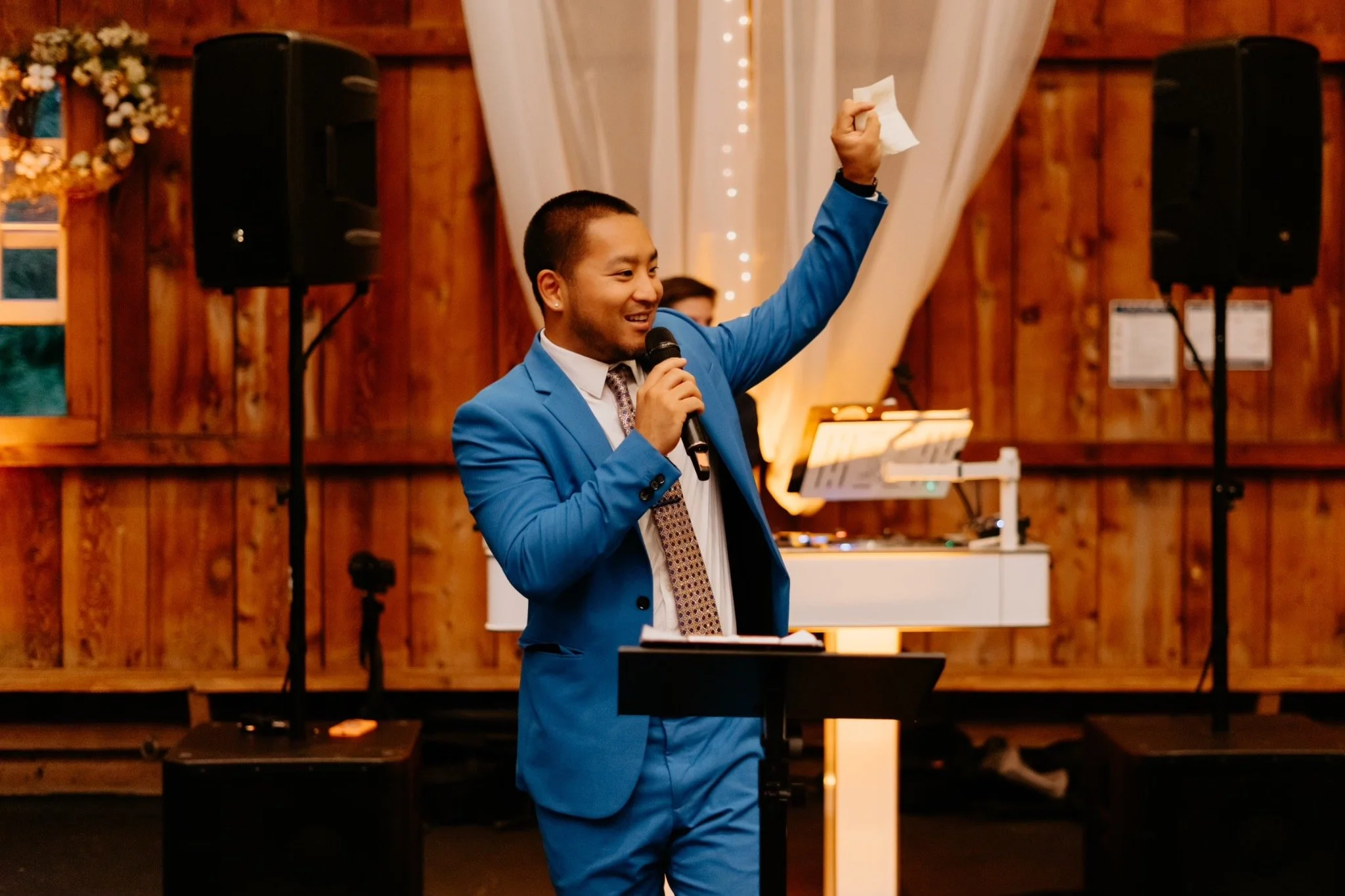 DJ Washburn hosting a wedding in a blue suit with a microphone and one arm raised