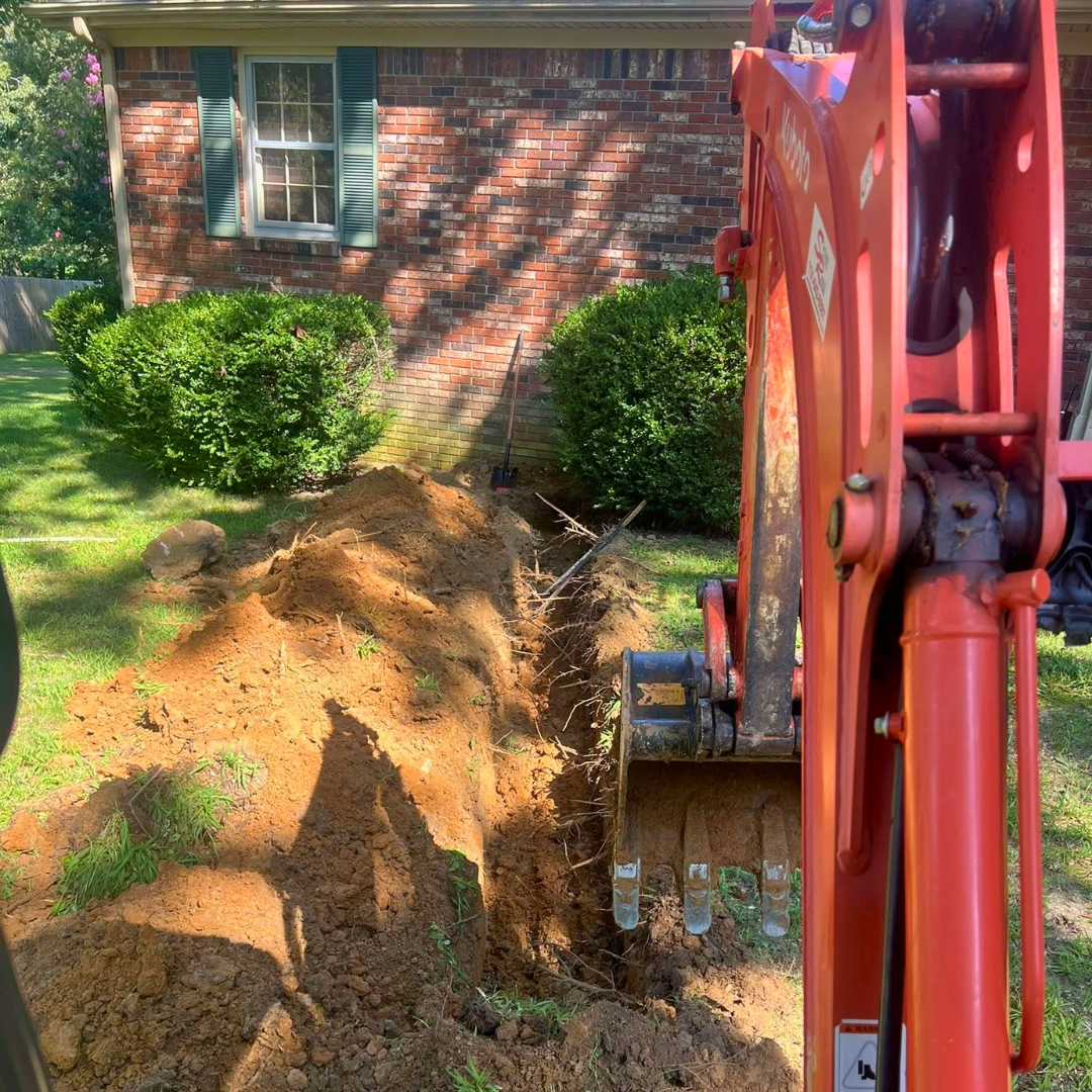 Mini excavator digging a water line beside a brick home