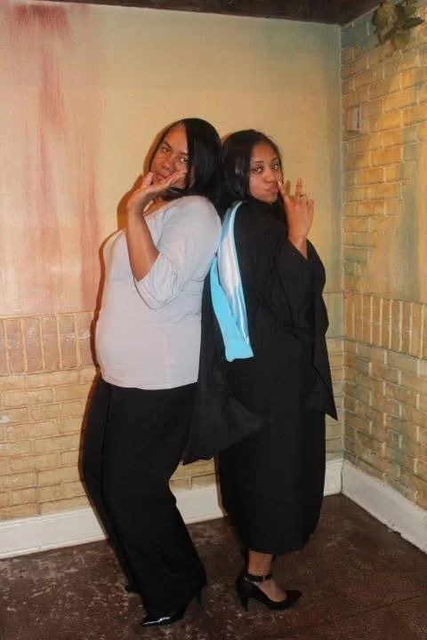 Chéla in graduation attire standing back to back with her aunt, Stephanie Hobbs, who is wearing a gray shirt