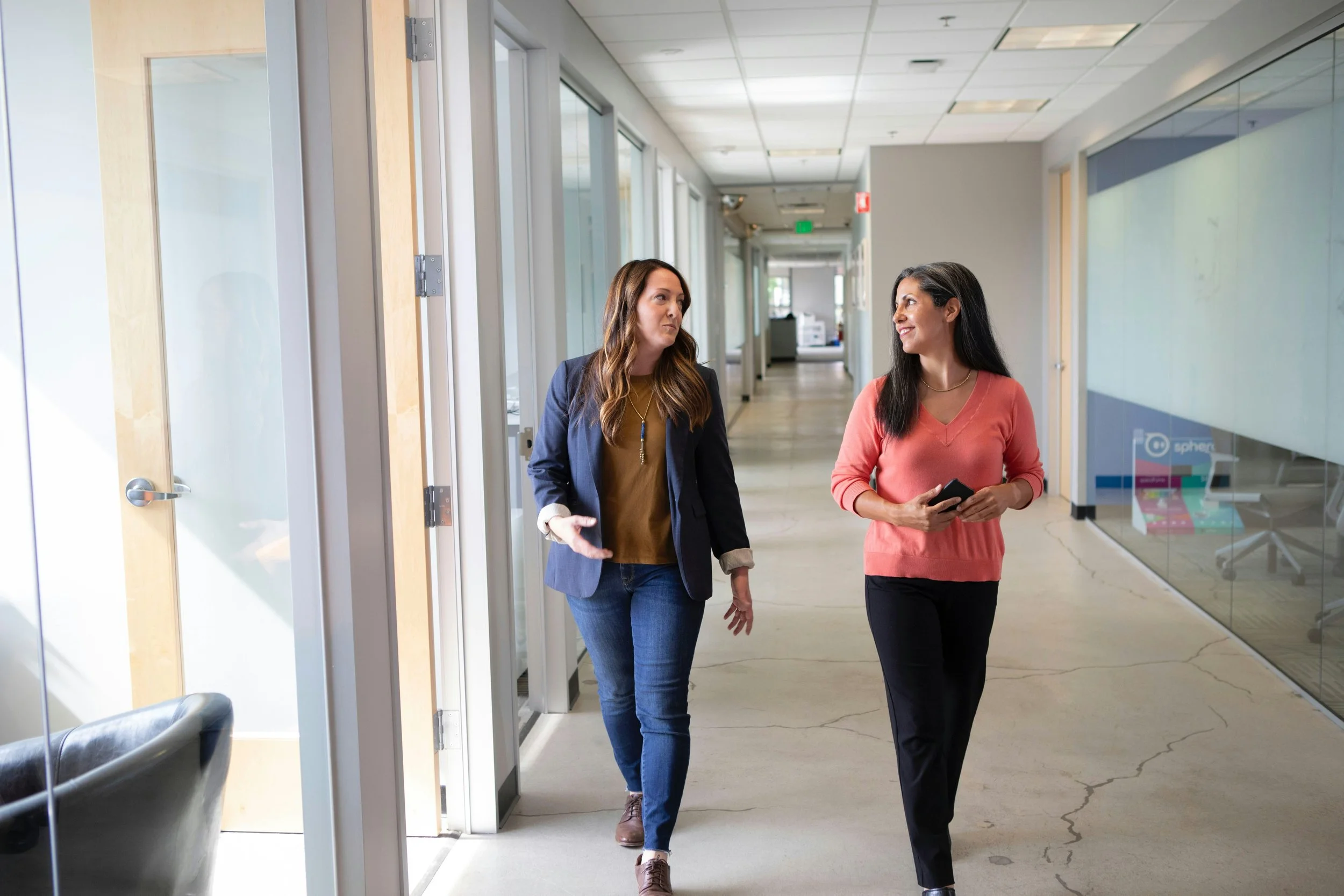 Two professional women talking while walking through an office