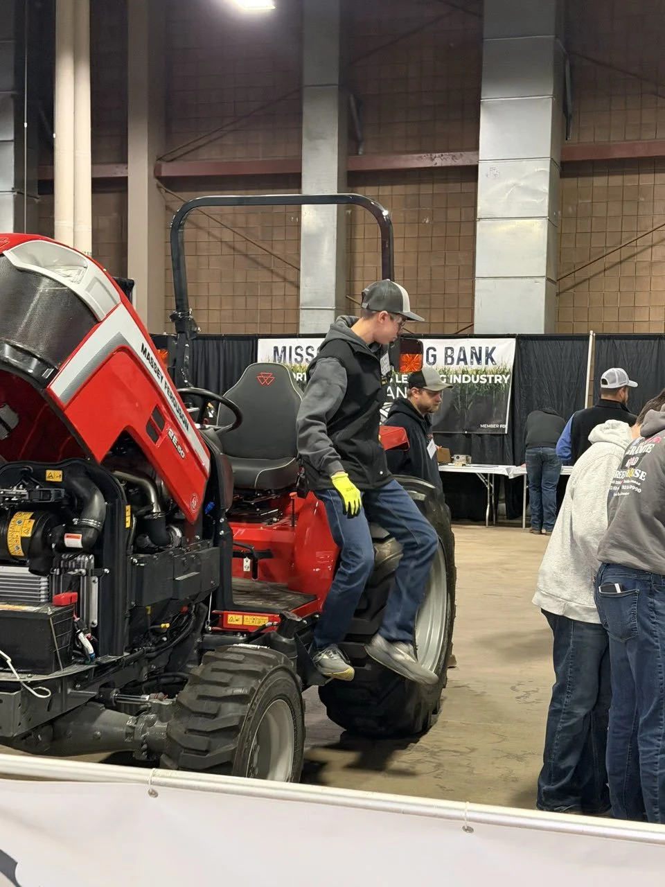A visitor at the controls of a red utility machine on a farm show floor