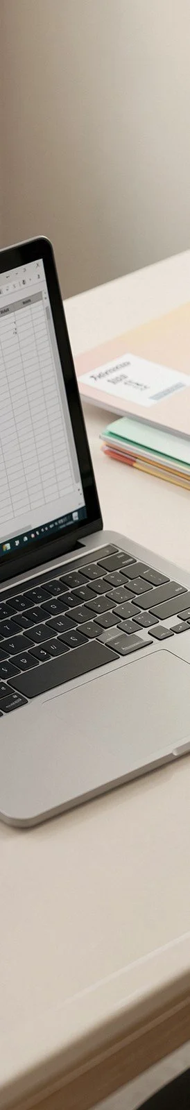 Laptop with a spreadsheet open next to notebooks