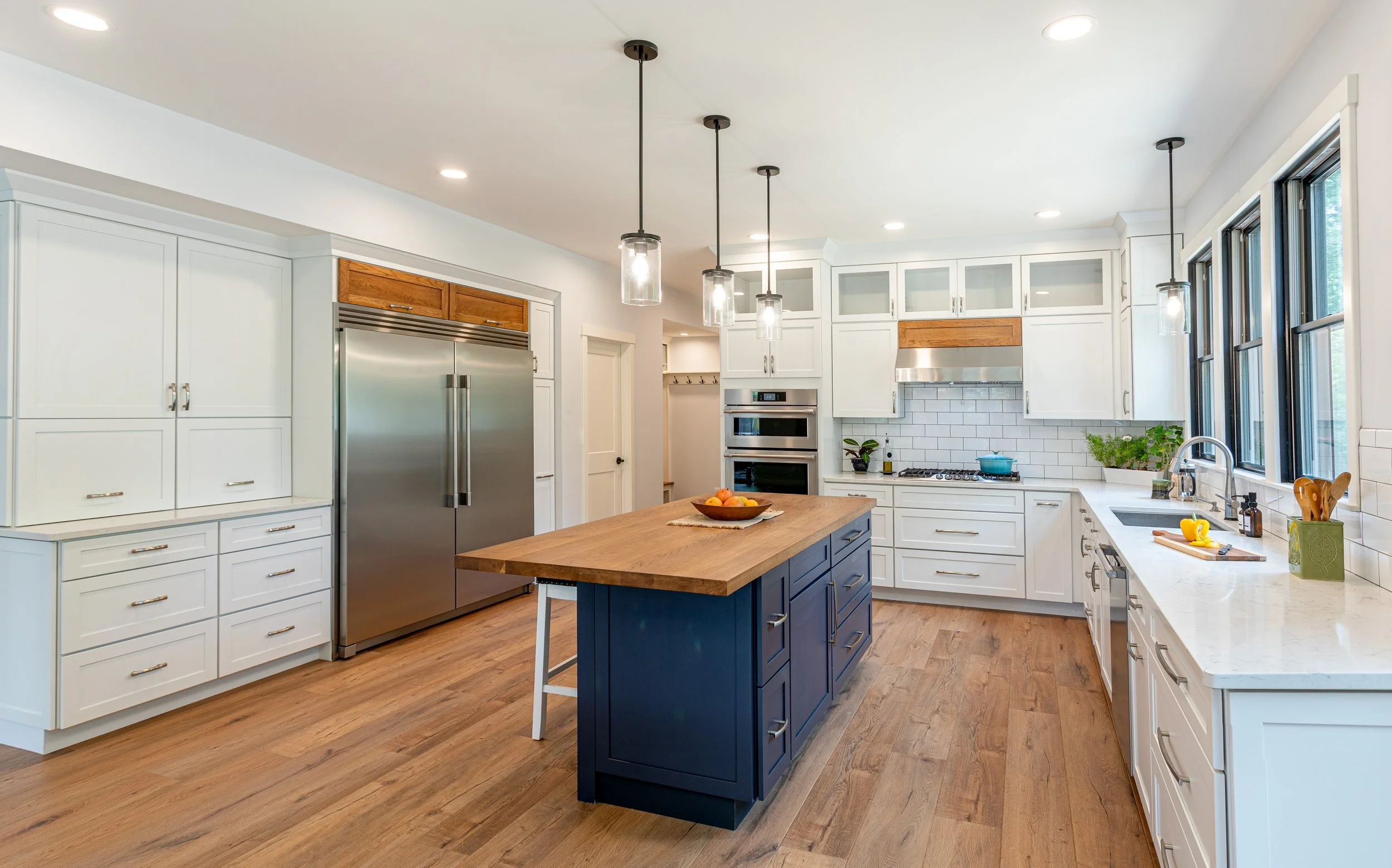 Remodeled kitchen with painted cabinetry, navy island with butcher block top, and glass-front uppers