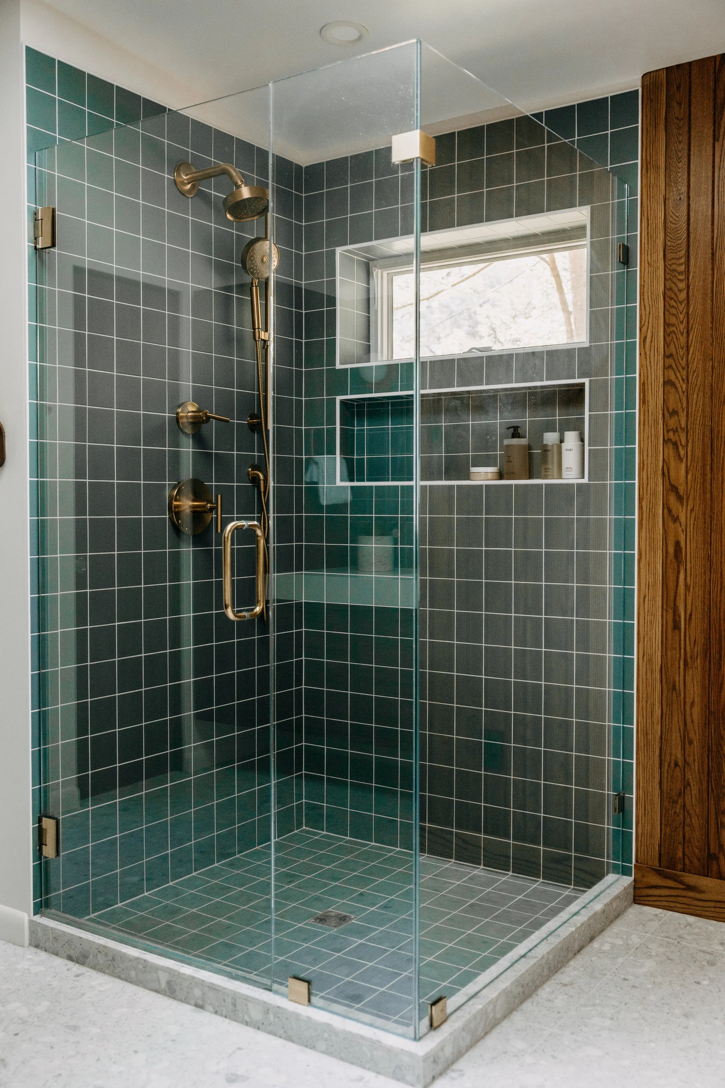 Tiled walk-in shower with glass enclosure and brass fixtures