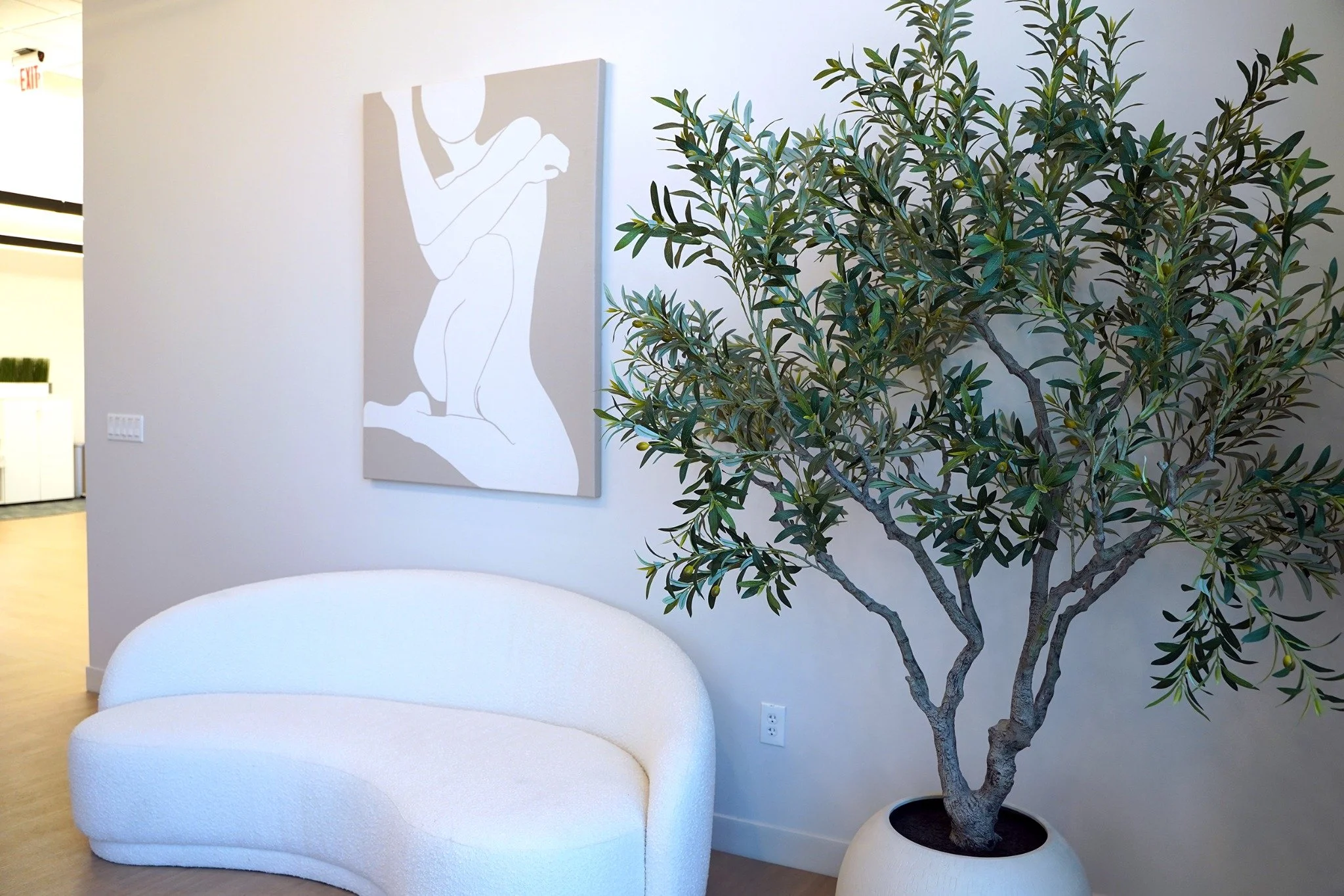 MNML Med Spa lobby with a curved cream chair, botanical greenery, and neutral artwork