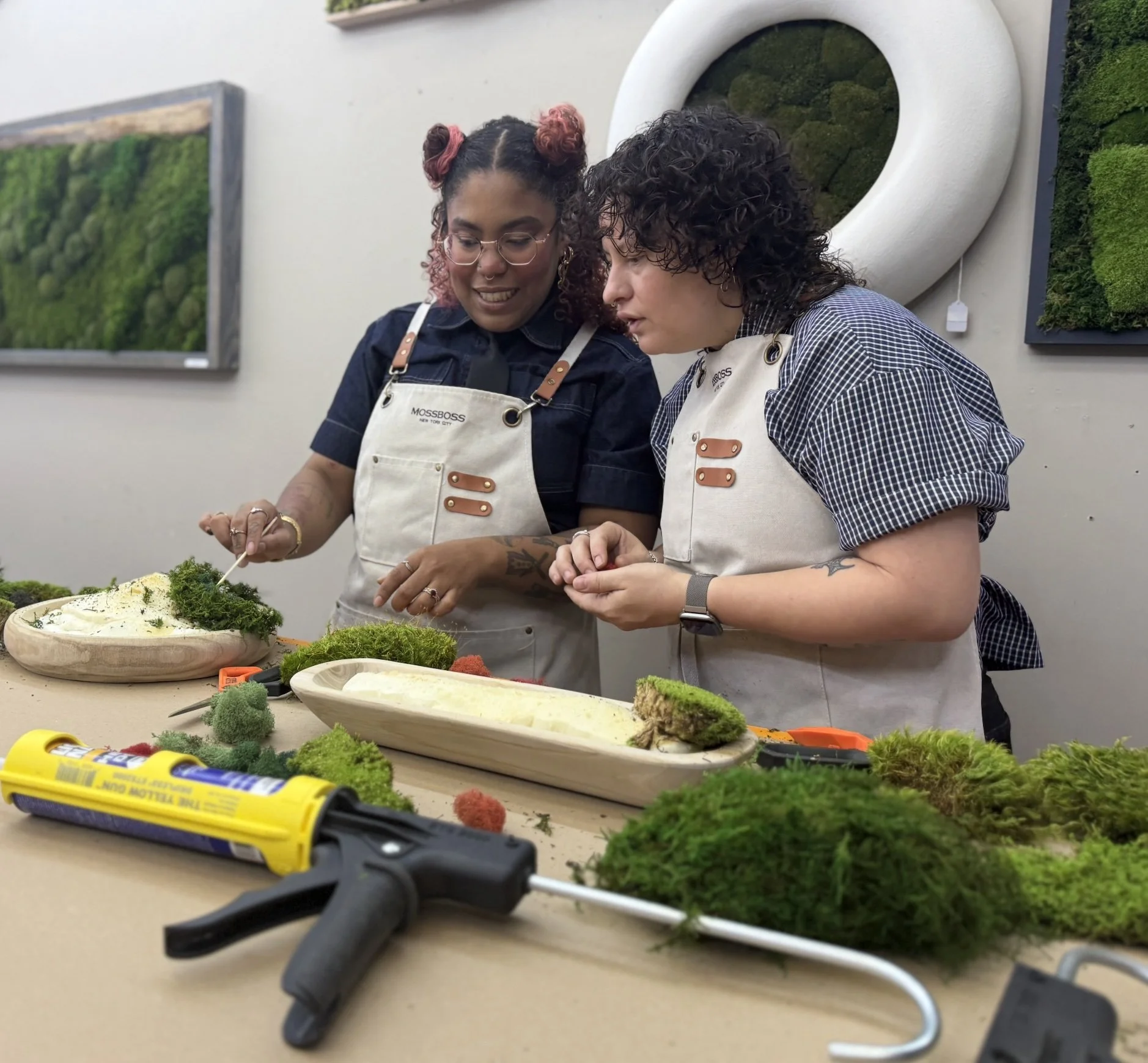 Kate and Vicky leaning in over their moss bowls, focused on placing accent moss