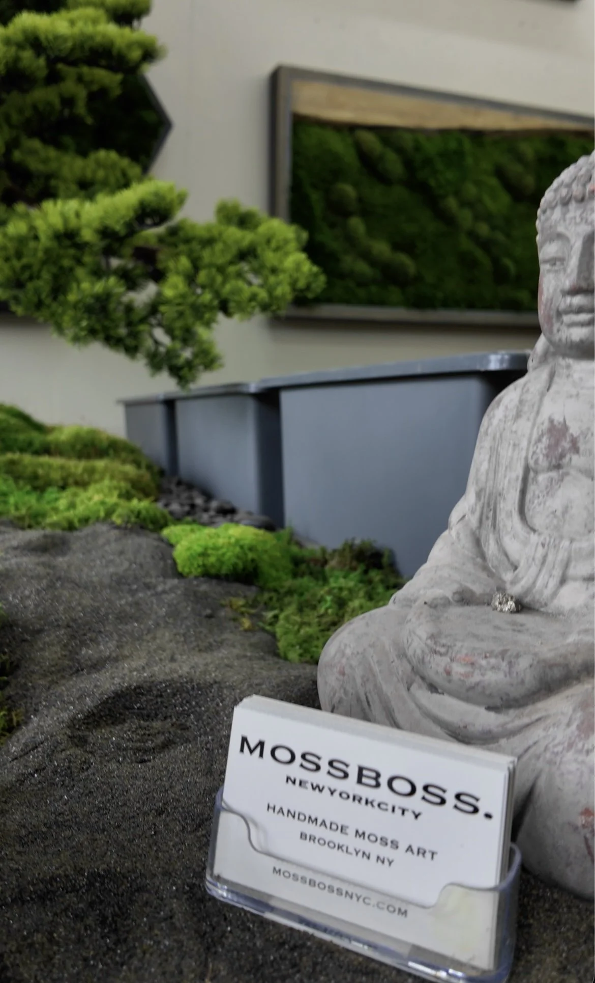 MossBoss business card resting near a stone Buddha statue and framed moss art inside the studio