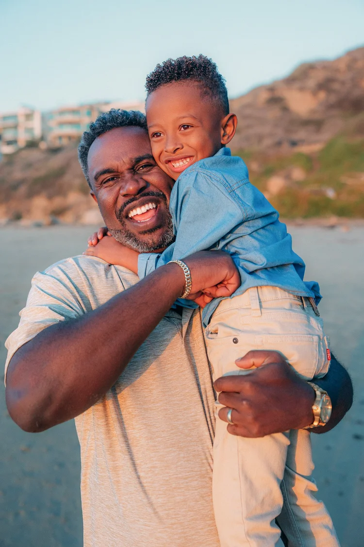 A father carrying his laughing son on his back on the beach