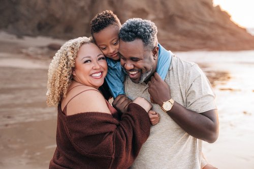 A mom and dad laughing with their son wrapped around dad's shoulders at Strands Beach in Dana Point