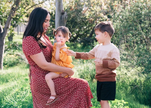 A mom holding her toddler daughter while her son reaches up to her among the greenery at William R. Mason Regional Park in Irvine