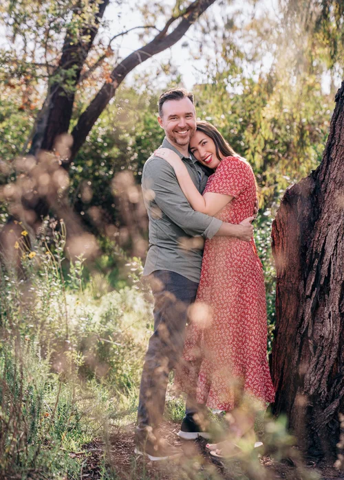 Mom and Dad wrapped up in each other beside a eucalyptus trunk, both smiling at the camera
