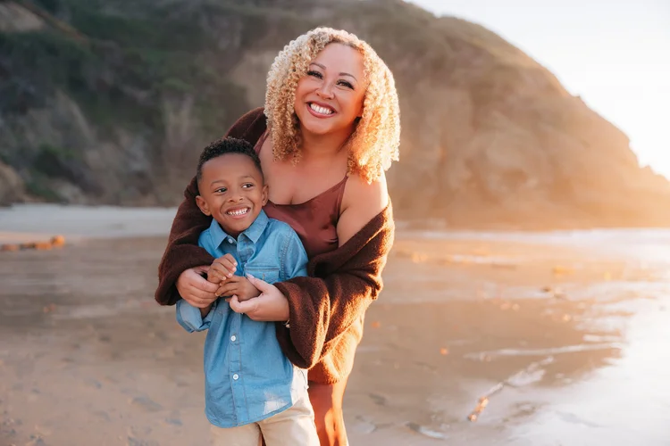 A mother wrapping her arms around her young son on the beach at sunset