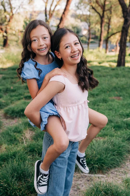 The older Slemmons sister carrying her little sister piggyback across the grass, both laughing
