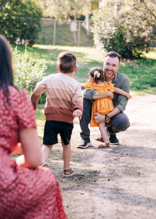 Their son running down the path toward Dad, who is crouched waiting with his sister in his arms