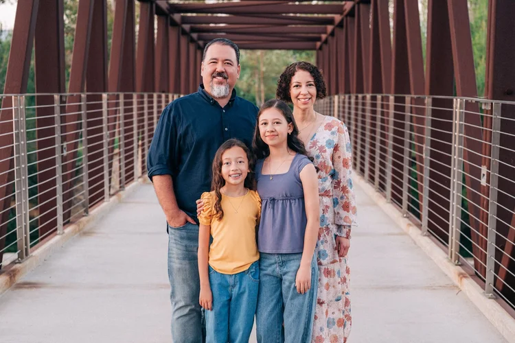 A family of four standing together for a classic portrait on a trail bridge in Orange County