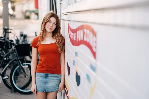A senior in an orange tee against the red Fun Zone lettering on a boardwalk wall at the Balboa Fun Zone