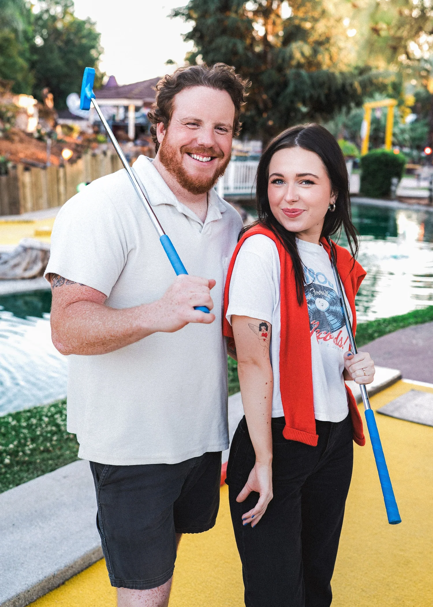 Hannah and Tylor back to back on a mini golf green, each holding a putter over a shoulder and grinning
