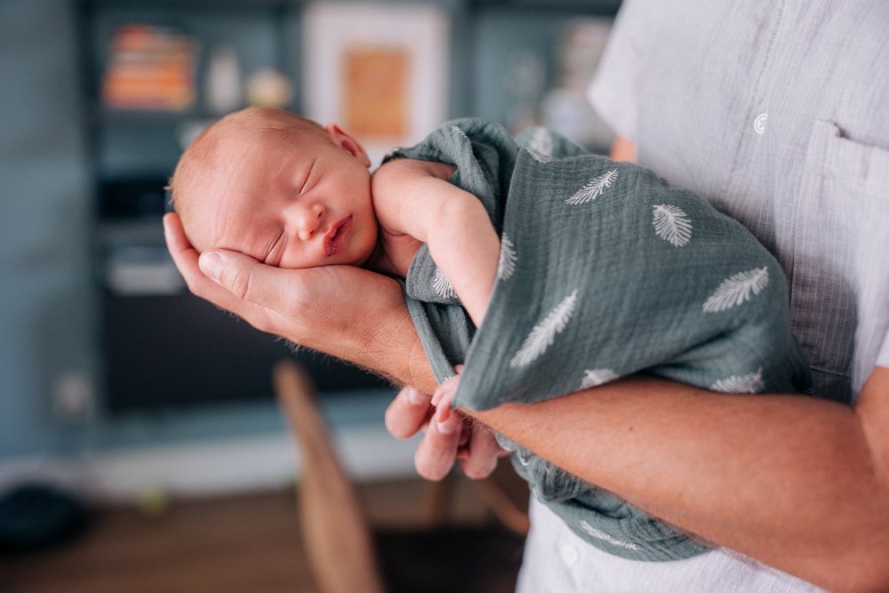 A swaddled newborn asleep along Dad's forearm