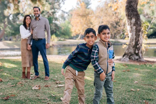 Two brothers grinning arm in arm with their parents behind them under the fall trees at Yorba Regional Park