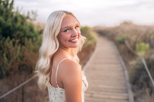 A senior smiling back over her shoulder on the boardwalk trail at Crystal Cove, the path curving away behind her