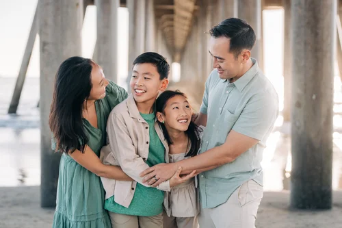 A family of four laughing together in the pilings under the Huntington Beach Pier